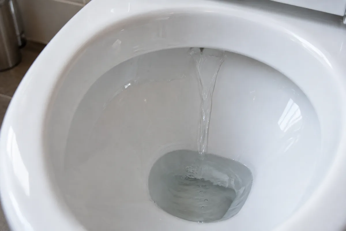 Filet d&rsquo;eau coulant en continu le long de la paroi d&rsquo;une cuvette de WC blanche