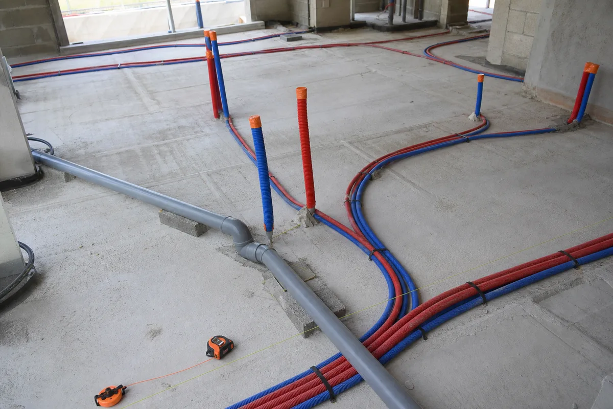 Réseau de plomberie en attente sur une dalle de chantier, tubes gainés et attentes repérées avant coulage de la chape